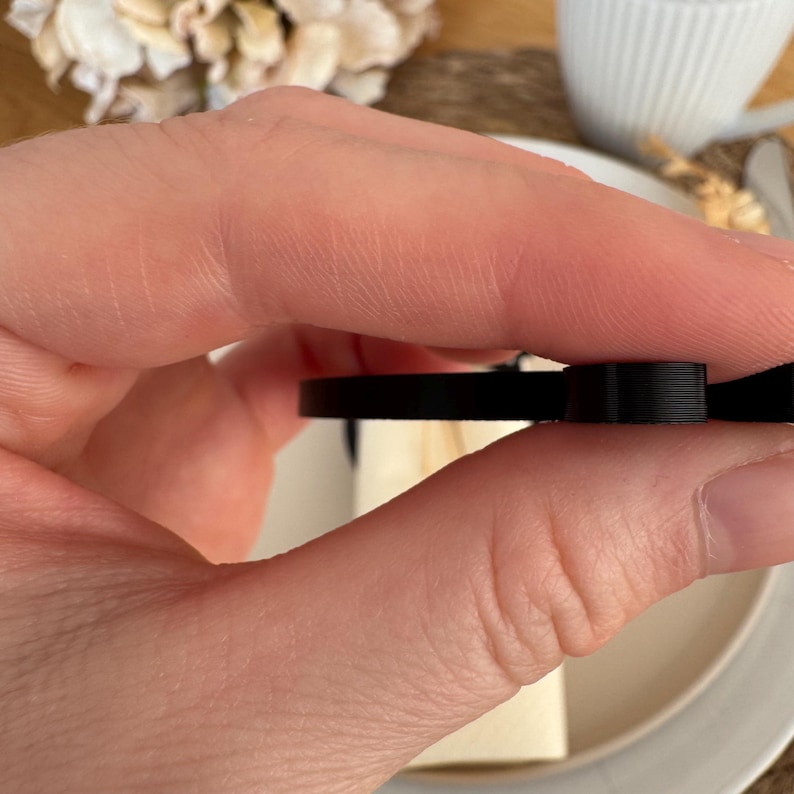 Op de afbeelding: Een zwarte plastic strik met een glad, afgerond oppervlak. De strik wordt in een hand gehouden.