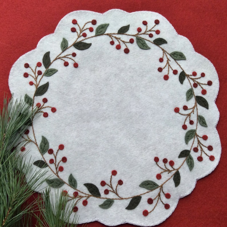 Puede incluir: Caminito de mesa de fieltro blanco con borde festoneado y un dise&ntilde;o bordado de hojas verdes y bayas rojas.