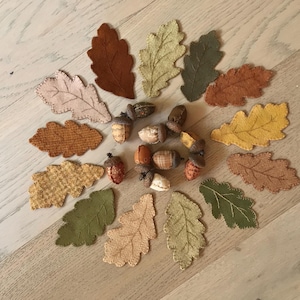 May include: A collection of autumn-themed decorative items, including fabric leaves in various colors like brown, green, and yellow, and several acorns. The leaves are arranged in a circular pattern, suggesting a fall harvest theme.