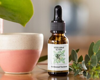 Puede incluir: Una botella de vidrio marrón con un gotero y una etiqueta blanca que dice "Wildcrafted by myAd Goldenrod Tincture 2 oz (57 gr)". La etiqueta también presenta una ilustración dibujada a mano de una planta de vara de oro.