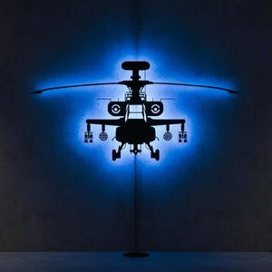 May include: A dark silhouette of a helicopter is illuminated with blue light against a gray wall. The room features framed artwork and a display screen with technical schematics. Additional model helicopters are on display.