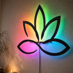 Può includere: Un'opera d'arte da parete a forma di fiore di loto nero con illuminazione a LED integrata che emette un vivace gradiente di colori, tra cui rosso, giallo, verde e blu. Il design è composto da linee curve e include un cavo di alimentazione nero.
