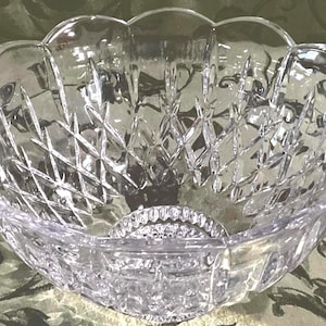 May include: A clear, decorative crystal bowl with a scalloped rim and diamond-cut pattern. The bowl has a circular base with a detailed design. This elegant bowl is suitable for serving or display.