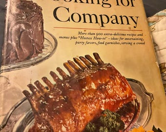 May include: A vintage cookbook titled "Cooking for Company" by the Food Editors of Farm Journal. The cover features a chocolate cake and a roasted rack of lamb.