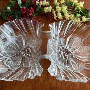 May include: A clear glass serving dish with two sections, each shaped like a flower with a raised design. The dish is ideal for serving snacks or appetizers.