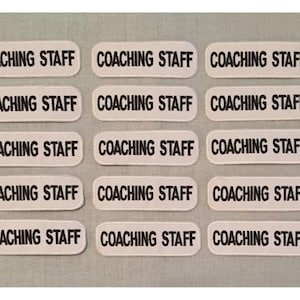 May include: Fifteen white rectangular labels with black text that reads "COACHING STAFF".