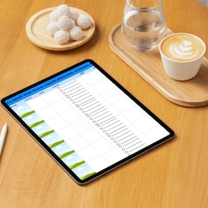 Puede incluir: Una tableta con un planificador digital en blanco en la pantalla. La tableta está sobre una mesa de madera con una taza de café, un vaso de agua y un pequeño plato de trufas de chocolate blanco.