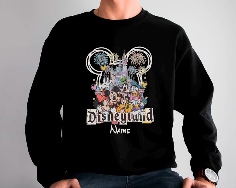 May include: Black sweatshirt featuring a colorful Disneyland graphic with Mickey Mouse, Minnie Mouse, Donald Duck, and other characters. The design includes fireworks, a castle, and the text "Disneyland" and "Name".