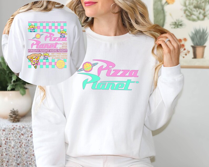 May include: White sweatshirt featuring the Pizza Planet logo in pink and teal. The design includes a planet graphic and the text "Pizza Planet". The back of the sweatshirt has additional graphics and text, including a pizza slice and alien characters.
