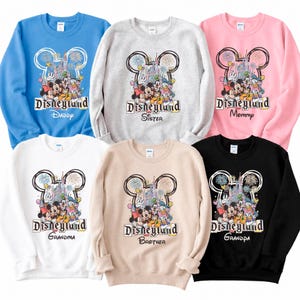 May include: Six crew neck sweatshirts in various colors, including blue, gray, pink, white, tan, and black. Each sweatshirt features a Disneyland graphic with Mickey Mouse and friends, and the words "Daddy", "Sister", "Mommy", "Grandma", "Brother", and "Grandpa".