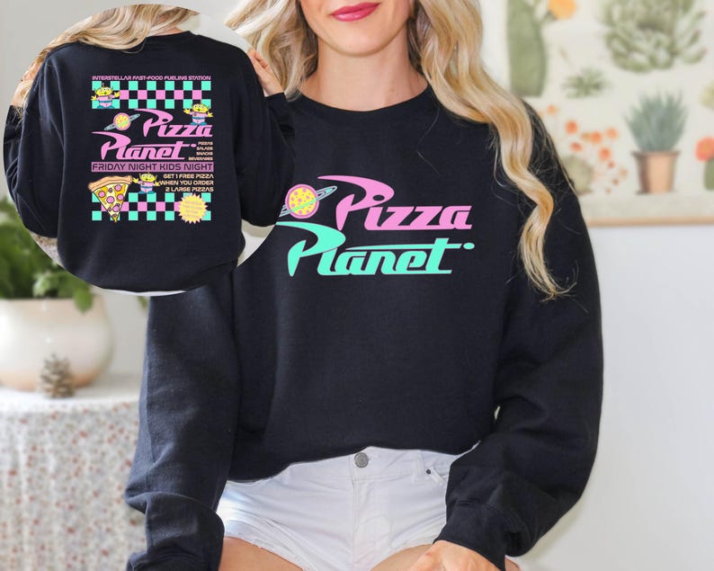 May include: Black sweatshirt with the words "Pizza Planet" in pink and teal. The back of the sweatshirt features the text "Interstellar Fast Food Airline Station" and "Friday Night Kids Night". The design includes pizza slices and alien characters.