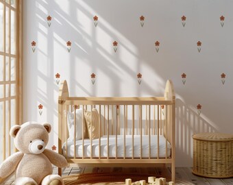 May include: A light wood baby crib with a white mattress and pillows, a teddy bear, and a woven basket. The wall is decorated with orange flower decals. A round rug and wooden blocks are on the floor.