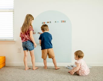 May include: A large, pale blue, arch-shaped wall decal applied to a white wall. The decal features a smooth surface where various colorful, small, magnetic-style alphabet letters are attached, including the characters A, B, C, M, R, N, I, X, and J.