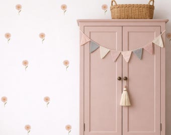 May include: A light pink cabinet with two doors, a woven basket, and a garland of pastel-colored pennants. The white wall is decorated with repeating floral decals. Wooden blocks are on the floor.