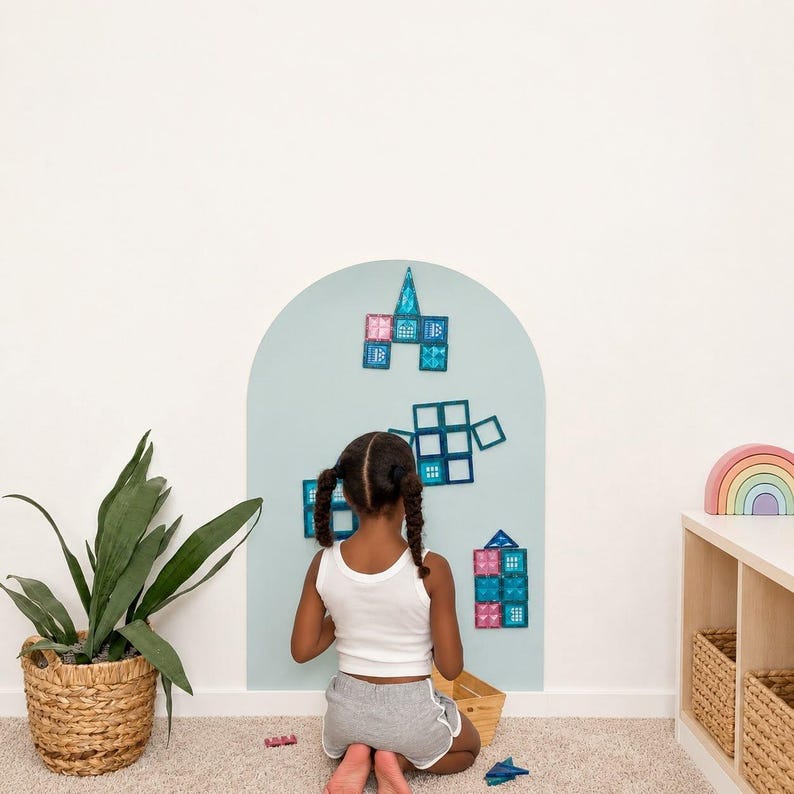 May include: A light blue arched wall decal featuring various translucent magnetic building tiles in shades of blue and pink arranged in geometric shapes. The tiles are attached to the surface, creating a colorful display of squares and triangles.