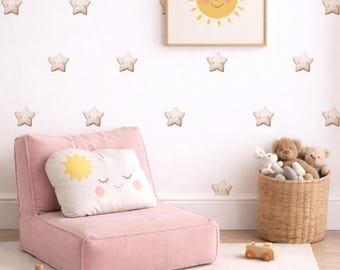 May include: A nursery scene with a pink floor chair, a white rug, and a framed sun illustration. The wall features star decals. A pillow with a sun and cloud design rests on the chair. A wicker basket holds stuffed animals, and wooden toys are on the floor.