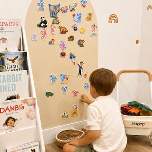 May include: A large beige wall-mounted arch display board featuring numerous colorful magnetic character cutouts, including animals, cartoon figures, and objects, arranged across the surface for interactive play and educational engagement.