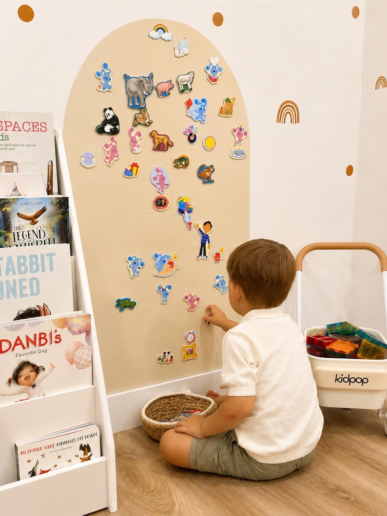 May include: A large beige wall-mounted arch display board featuring numerous colorful magnetic character cutouts, including animals, cartoon figures, and objects, arranged across the surface for interactive play and educational engagement.