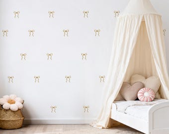May include: A child's bedroom with a white bed, canopy, and decorative pillows. The white wall features gold bow decals. A woven basket with a flower-shaped pillow and a round rug complete the room's decor.