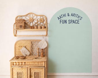 May include: A rattan play kitchen with a matching wall shelf and a large, light green arch-shaped wall decal featuring the dark blue text AATHI & ARITH'S FUN SPACE. The kitchen includes two cabinet doors, knobs, and a lattice-patterned back panel.