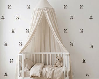 May include: A white crib with a beige canopy and bedding. The wall is decorated with panda bear decals. A stuffed teddy bear sits on the bed, creating a cozy nursery setting. The room has a soft, neutral color palette.