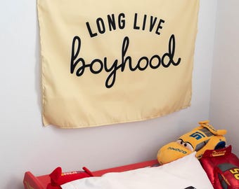 May include: A yellow wall tapestry with black text that reads "Long Live Boyhood". The tapestry is hanging on a white wall above a red race car bed with a white and red pillow with the text "Lightning Speed".