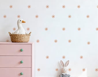 May include: A pink dresser with three drawers and mint green knobs. A white stuffed duck sits in a woven basket on top of the dresser. A stuffed bunny in a plaid dress sits on the floor. The white wall has a pattern of peach-colored flower decals.