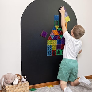 May include: A large arched black wall decal featuring a collection of colorful, translucent magnetic building tiles arranged in a house-like structure. The tiles are square and triangular in shades of red, blue, green, orange, purple, and yellow.