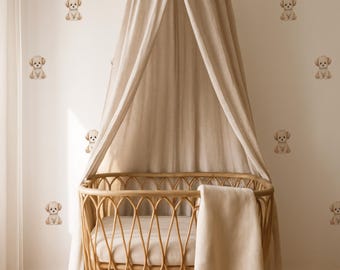May include: A nursery scene featuring a light brown wicker crib with a canopy and a soft blanket. The walls are adorned with repeating watercolor illustrations of small puppies. The overall color palette is neutral, creating a calming and inviting atmosphere.