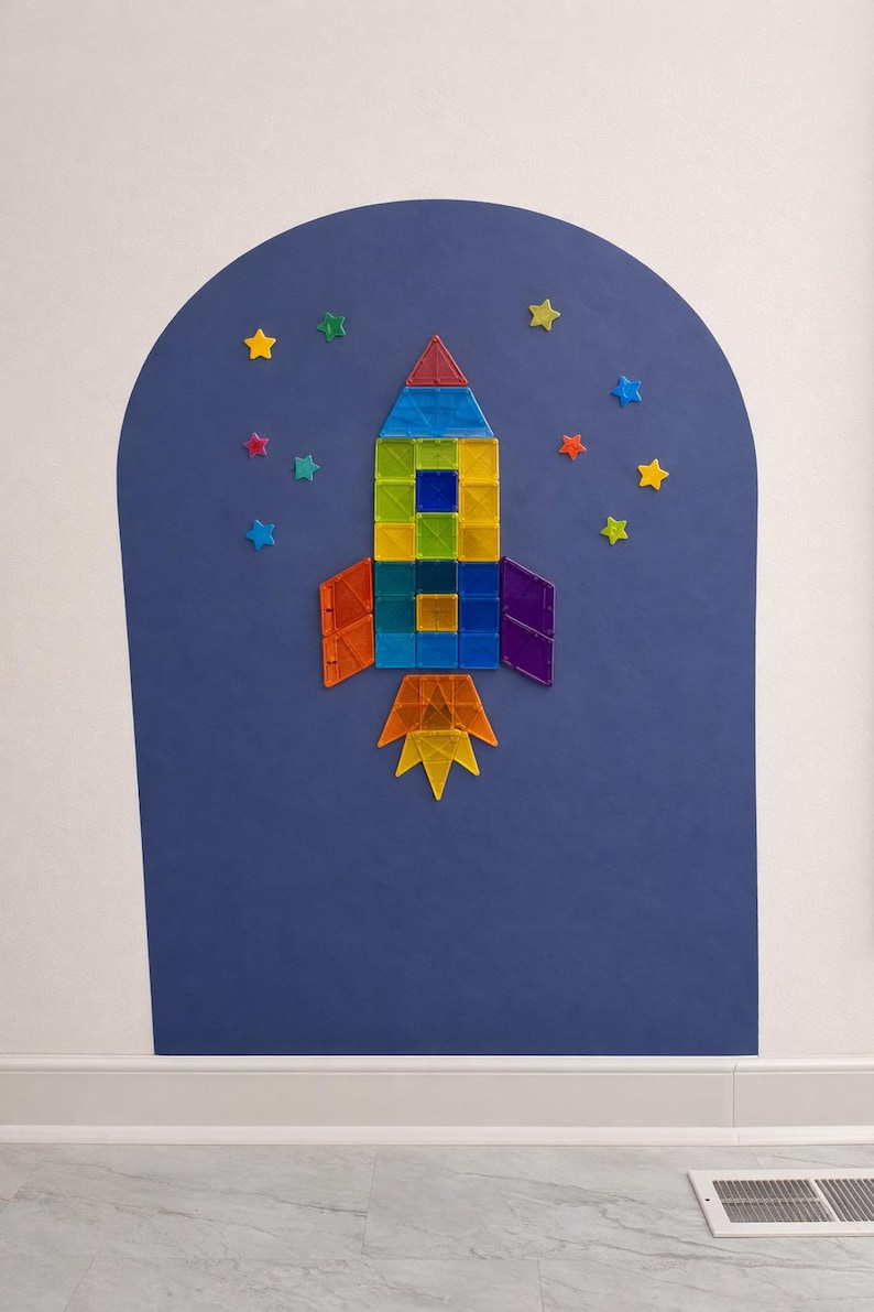 May include: A rocket ship constructed from colorful translucent magnetic tiles, featuring a red nose cone, a blue, green, and yellow body, orange and purple fins, and a yellow and orange flame, surrounded by small star-shaped magnetic tiles.