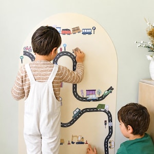 May include: A tall, arched, light-colored wooden wall panel featuring a printed black road map graphic with various vehicles, traffic signs, and buildings. The design includes a train at the top and construction equipment at the bottom.