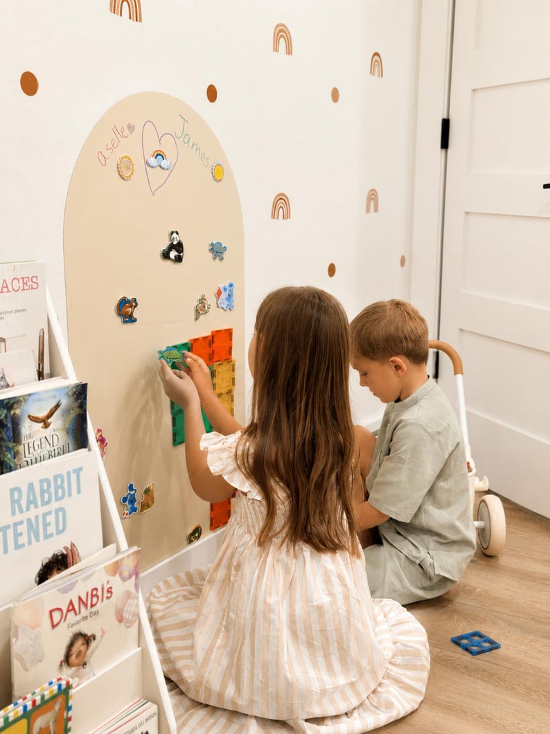 May include: A large, beige, arch-shaped magnetic wall board featuring a hand-drawn heart with the names "a selle" and "James" written inside. The board is decorated with various small magnetic figures, including a panda and a squirrel.