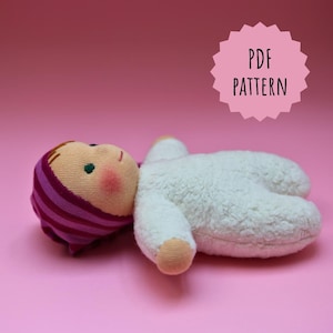 May include: A white plush doll with a pink and purple striped hat. The doll has a painted face with green eyes and rosy cheeks. The doll is lying on a pink surface. PDF PATTERN.