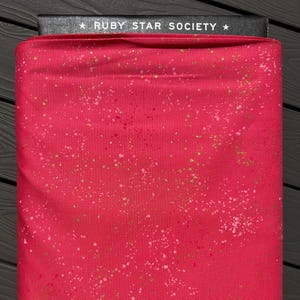 Peut inclure: Un rouleau de tissu rouge vif orné d'un motif moucheté composé de points dorés métallisés et rose clair. Le bord supérieur du tissu est fixé par une étiquette noire portant le texte blanc RUBY STAR SOCIETY et deux étoiles.