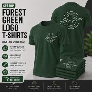 May include: Forest green short-sleeve t-shirts featuring a white circular logo with the text Art n Promo. The display includes one shirt shown from the front, one from the back, and a stack of folded shirts, all with the same white graphic print.