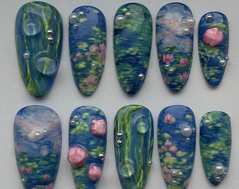 May include: Ten long, oval-shaped fake nails with a blue and green water lily design. The nails are decorated with silver and white beads.