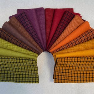 May include: A fan-shaped arrangement of folded fabric swatches in a spectrum of colors including olive green, lime, brown, purple, red, orange, and yellow. Some swatches feature a solid textured weave, while others display a black grid pattern.