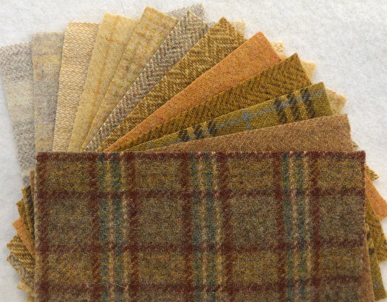 May include: A collection of 12 wool fabric squares in various shades of brown, beige, and gray. The squares are arranged in a fan shape, with the largest square at the bottom and the smallest square at the top. The fabric has a variety of textures, including smooth, textured, and patterned.