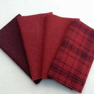 Puede incluir: Cuatro muestras de tela dobladas en tonos rojos. Los patrones incluyen espiga, un pequeño cuadro, un sólido y un diseño a cuadros. Las telas están dispuestas en forma de abanico, mostrando la variedad de texturas y patrones.