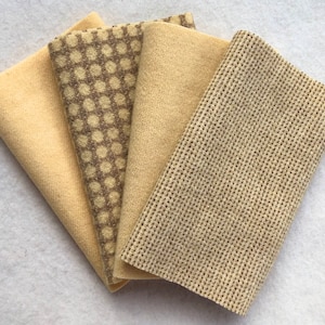 May include: Four pieces of fabric in shades of beige and brown. One piece has a small geometric pattern, another has a larger geometric pattern, and the third has a woven texture. The fourth piece is a solid beige color.