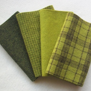 May include: Four green fabric swatches in varying shades and patterns. The swatches include a dark green herringbone, a lighter green plaid, a solid lime green, and a green and brown plaid. The fabrics are arranged in a fan shape.