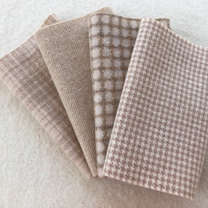 May include: A collection of folded fabric swatches in various neutral tones. The fabrics display different patterns, including herringbone, plaid, and houndstooth. The color palette consists of beige, tan, and off-white.