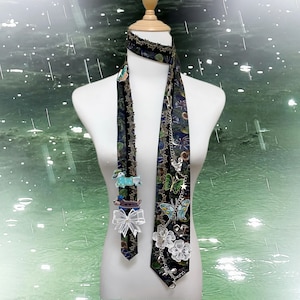 Può includere: Una cravatta fantasia con ciondoli decorativi, tra cui farfalle, fiori e cani bassotti. La cravatta è scura con un motivo floreale e di insetti, ed è esposta su un manichino.