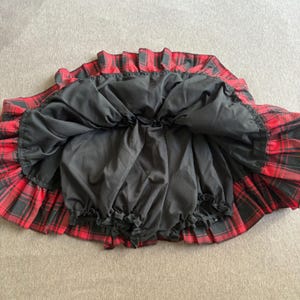 May include: A red and black plaid skirt with a black lining. The skirt is pleated and has a ruffled hem. The skirt is made of a lightweight fabric.