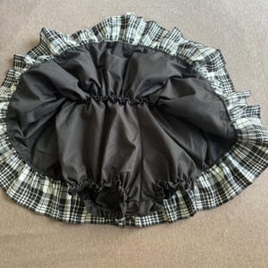 May include: A black and white plaid skirt with a ruffled hem. The skirt has a black lining and an elastic waistband. The skirt is designed to be worn as a petticoat or underskirt.