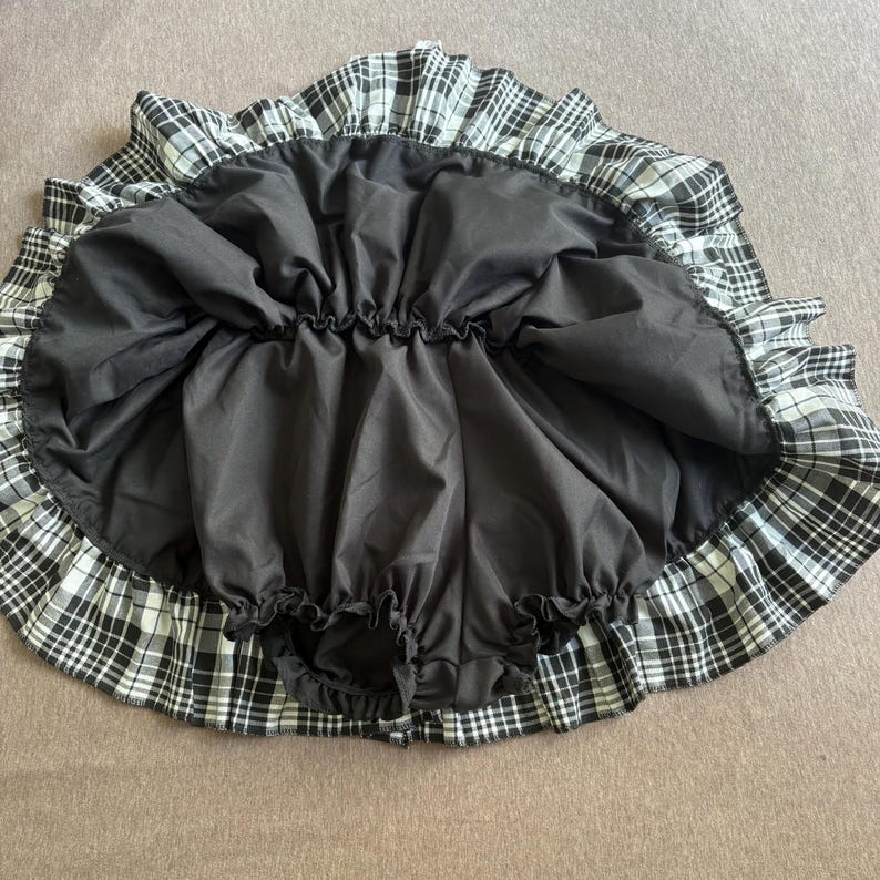 May include: A black and white plaid skirt with a ruffled hem. The skirt has a black lining and an elastic waistband. The skirt is designed to be worn as a petticoat or underskirt.