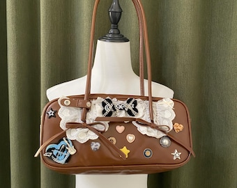 May include: A brown rectangular handbag with a top handle. The bag is decorated with white lace, bows, and various embellishments, including stars, hearts, and a blue and white design. The bag has a black bow in the center.