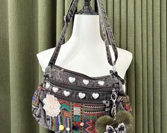 May include: A gray denim crossbody bag with multiple zippered compartments and white heart-shaped embellishments. The bag features a colorful embroidered panel and a fluffy green heart-shaped keychain with a bow. The bag is displayed on a mannequin.
