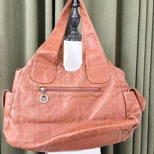May include: A large, brown leather tote bag with a zipper closure and two side pockets. The bag has a textured appearance and a silver charm on the zipper. The handles are wide and comfortable.