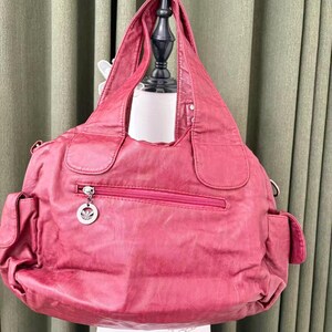 May include: A large, red handbag with a zippered pocket and two side pockets. The bag has a silver charm on the zipper and a shoulder strap. The bag is made of a soft, textured material.